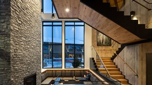 A modern interior with a stone wall, large windows, a wooden staircase, and a seating area. - Peaks Hotel & Suites (Banff)