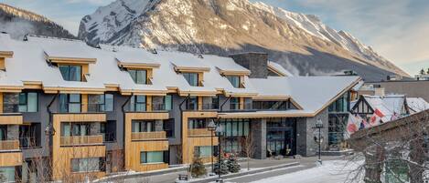 A modern hotel with multiple floors, large windows, and a mountain backdrop.