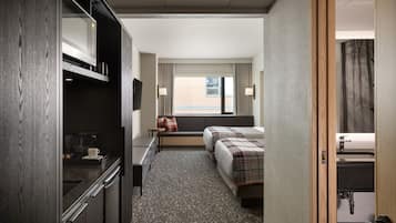 Habitación de hotel con kitchenette, cama con cubrecama escocés, ventana con cortinas y vista al exterior.