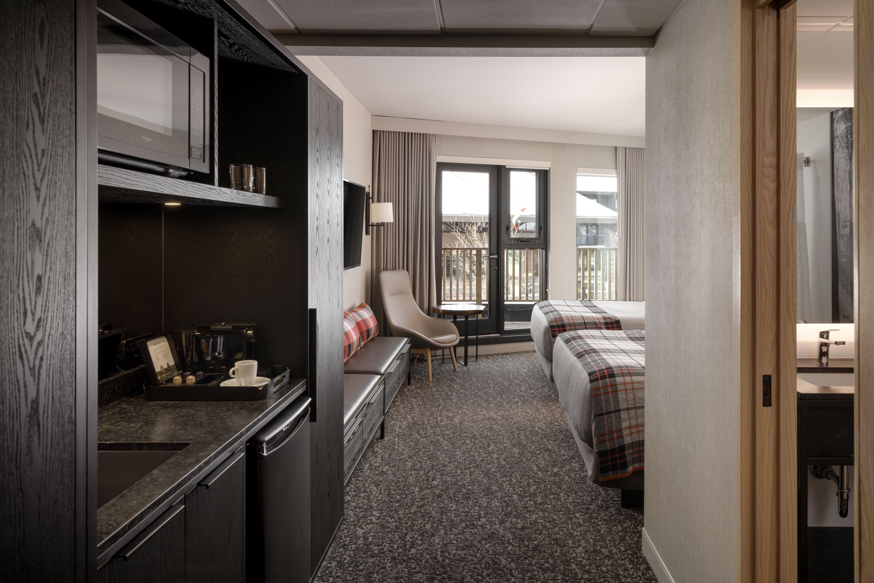 A hotel room with a kitchenette, a bed, a sofa, and a view of the outside.