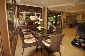 Uma sala de estar ampla com uma mesa de jantar de vidro, cadeiras de vime, televisão e um arranjo decorativo de orquídeas.