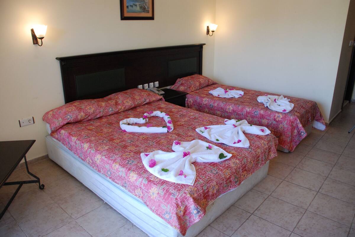 A hotel room with two beds, each with floral bedding and towels arranged on the beds.