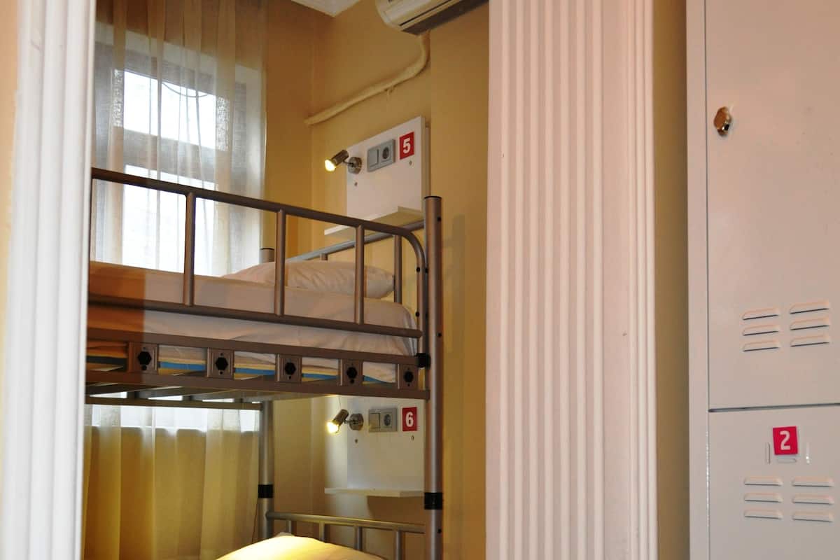 A bunk bed room with a window, a radiator, and a door with numbered lockers.