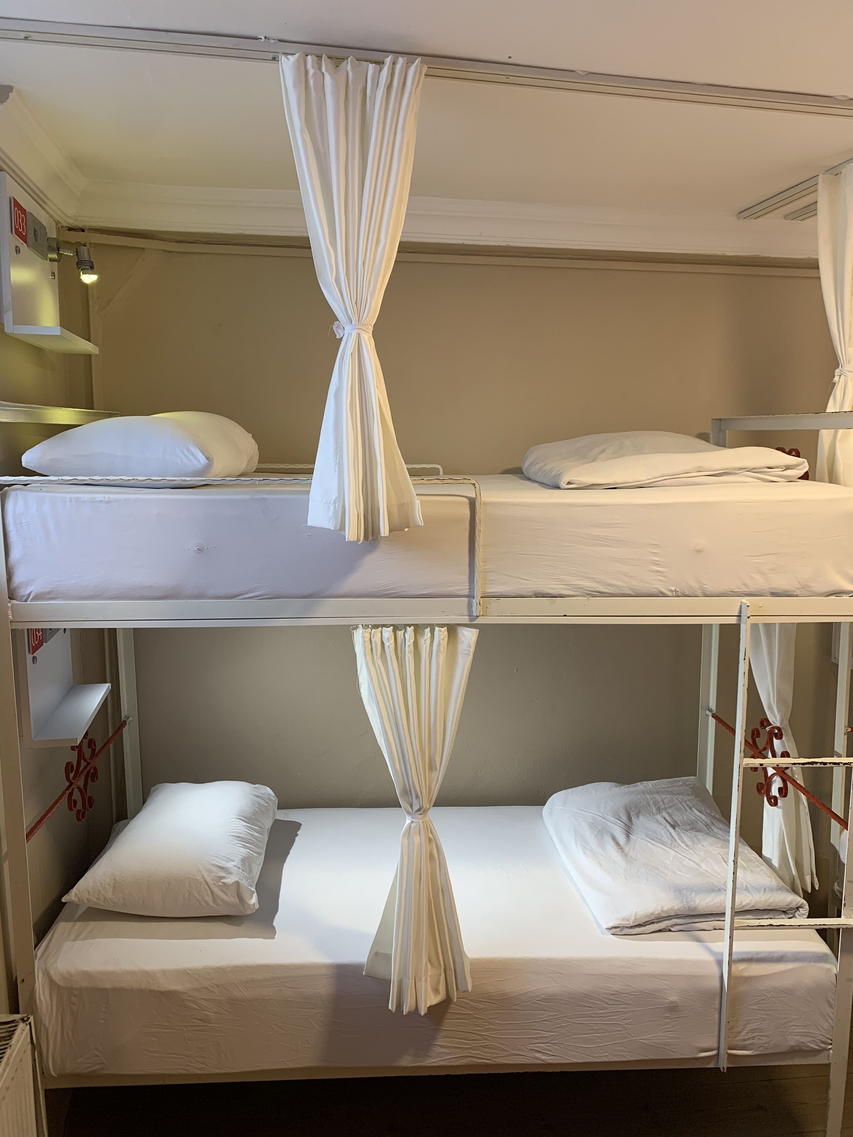 A bunk bed room with white bedding and curtains.