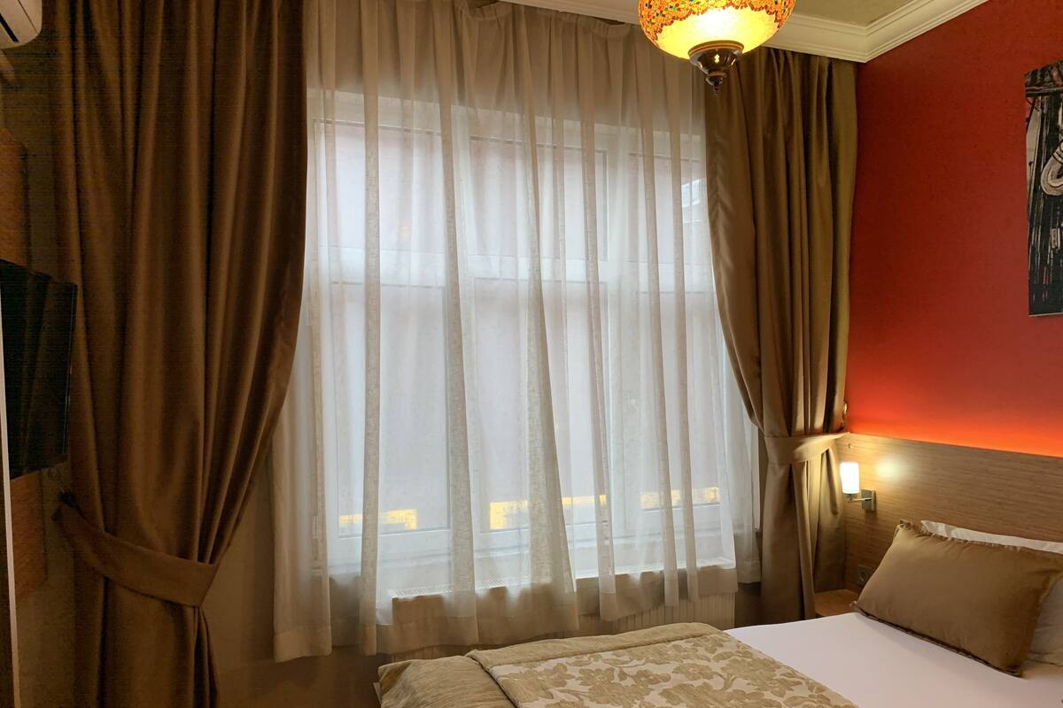 A hotel room with a bed, curtains, a nightstand, and a wall-mounted lamp.