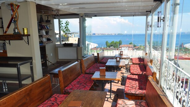 A restaurant with wooden benches and tables, a view of the sea, and a balcony with a railing. - Antique Hostel & Guesthouse (Istanbul)