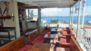 Un restaurante con bancos y mesas de madera, vistas al mar y un balcón con barandilla.