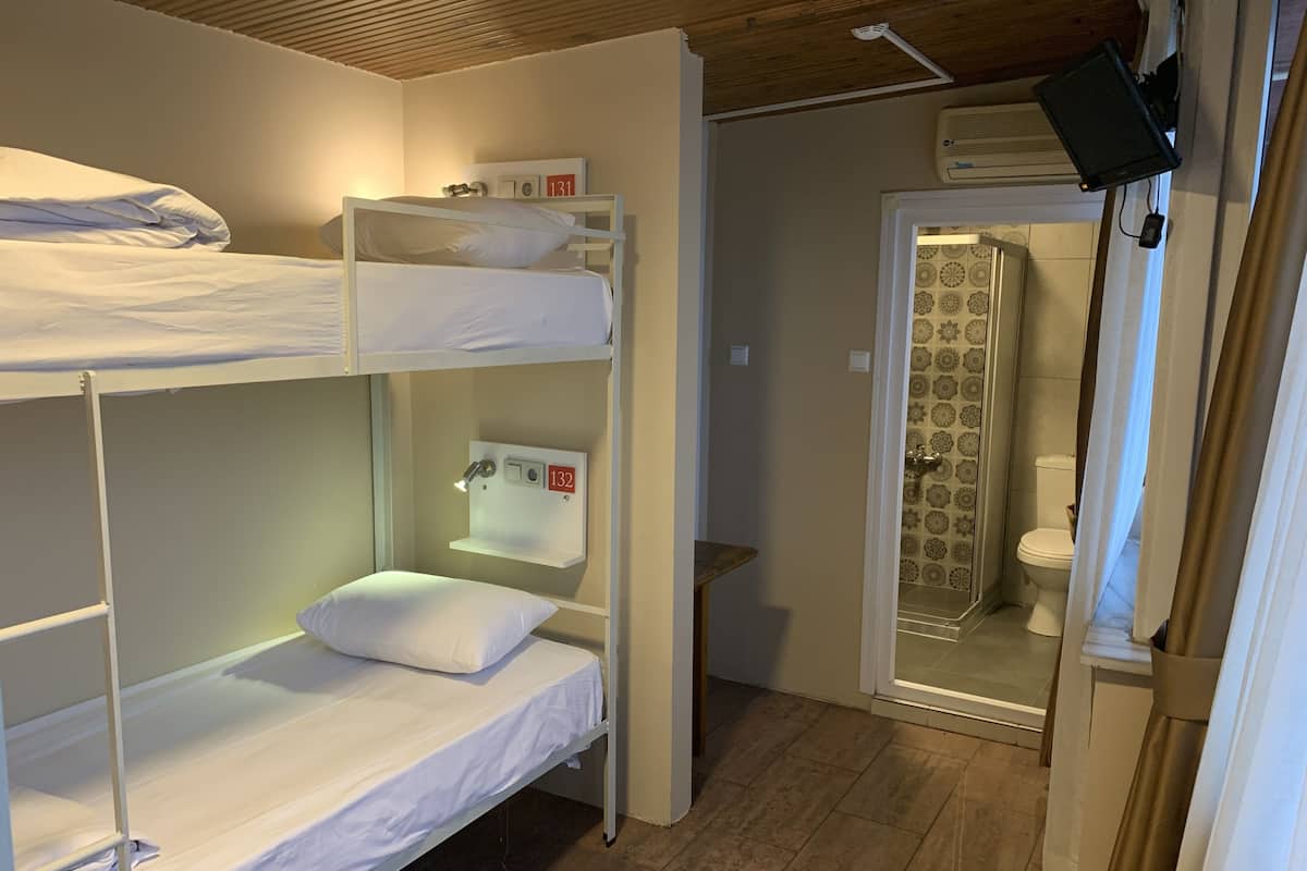 A bunk bed room with a small table and a shelf, a shower with patterned tiles, and a TV mounted on the wall.