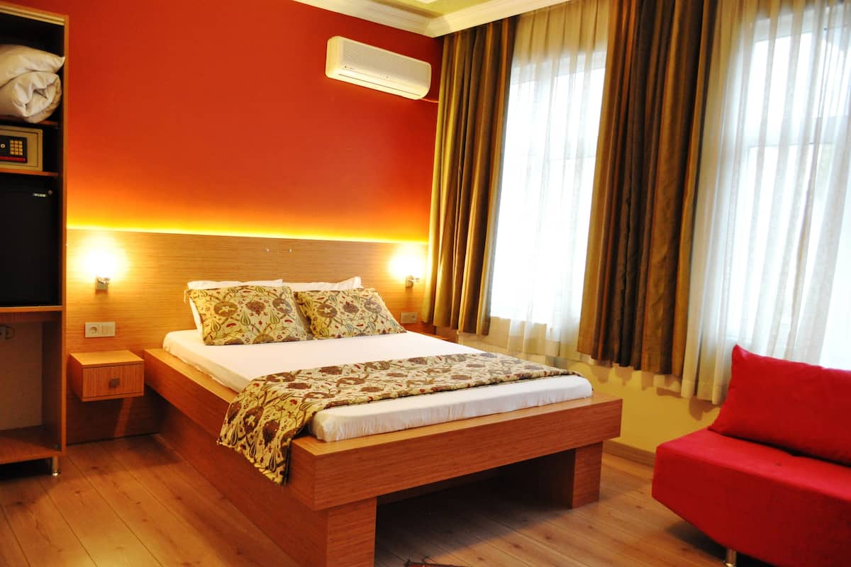 A hotel room with a wooden bed, a red armchair, and a nightstand with a lamp.