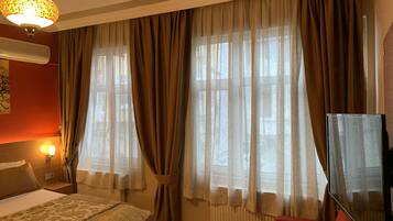 A hotel room with a bed, a red armchair, a TV, and large windows with curtains.