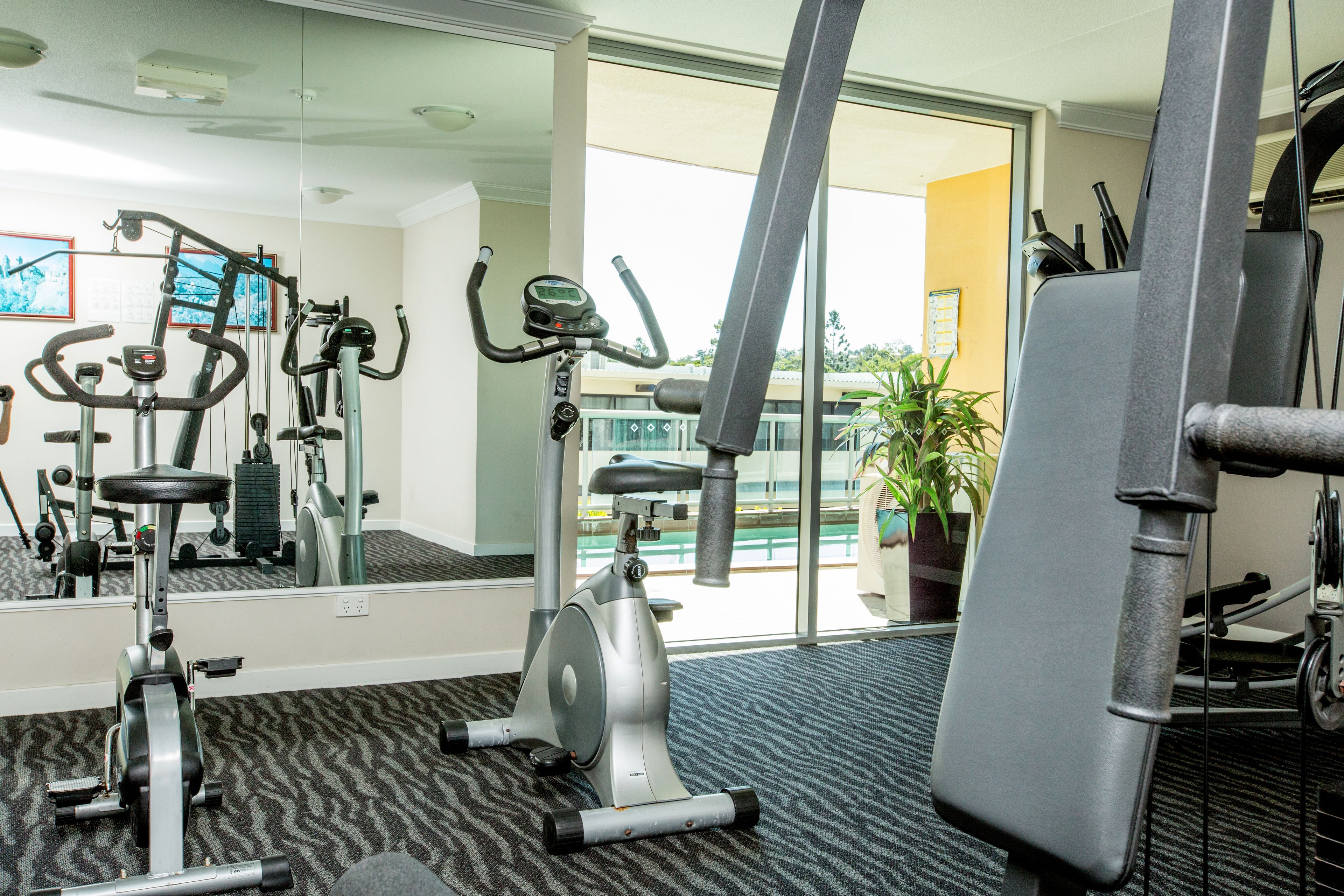 Un gimnasio con equipo de ejercicio, un espejo grande y vistas al exterior.