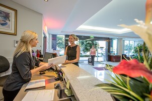 Una mesa de recepción con una recepcionista, una computadora y un mostrador con diversos objetos.