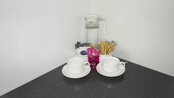 A coffee station with a coffee maker, two cups, and packets of coffee and creamer.