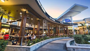 A modern shopping mall with a curved entrance, outdoor seating areas, and various retail stores.