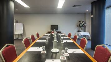 Un salón de conferencias con una larga mesa, sillas rojas, una pizarra y una pantalla de televisión.