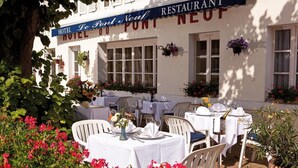 Restaurante de hotel con terraza, mesas y sillas blancas, rodeado de follaje y flores.