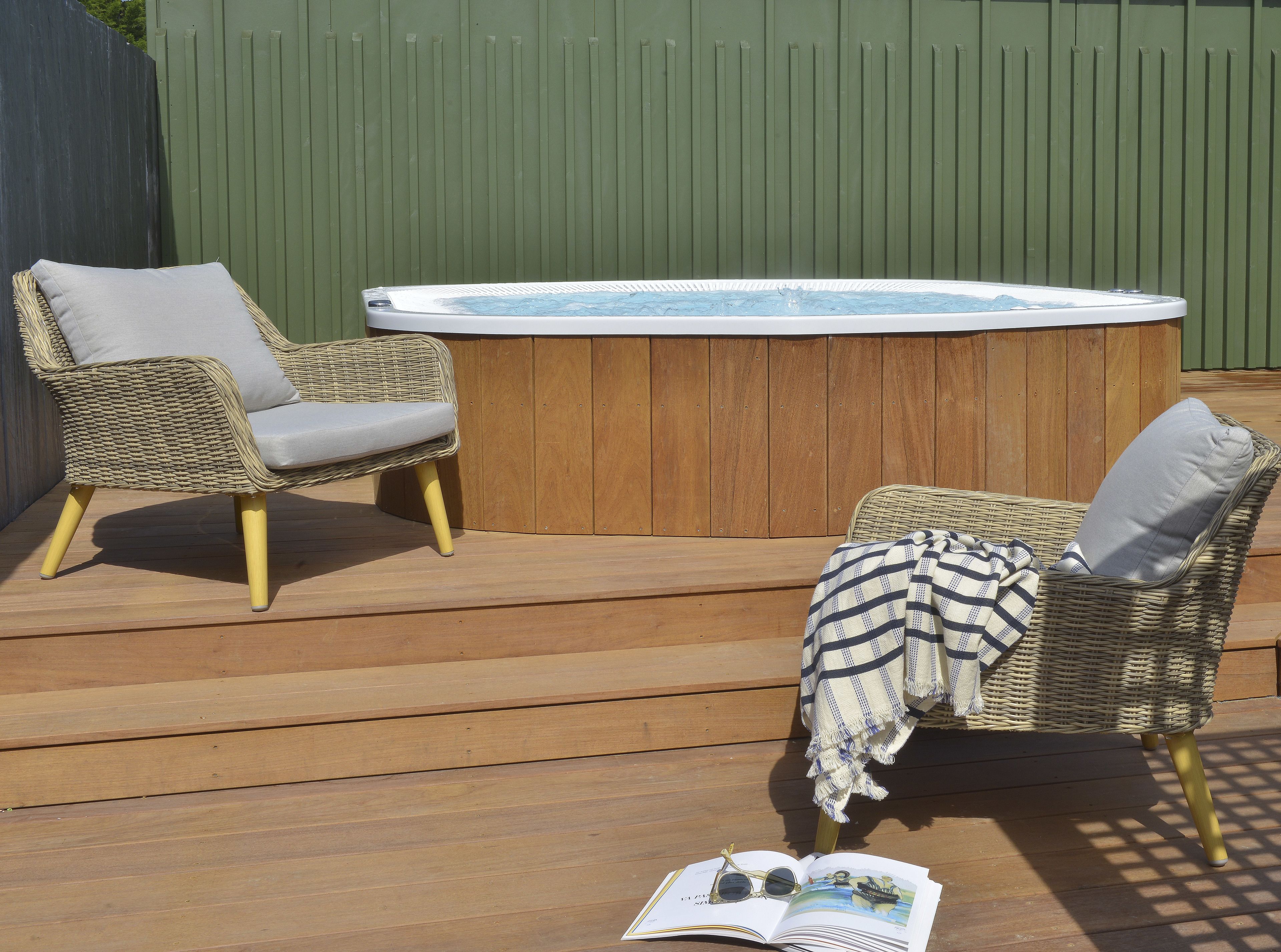 A wooden deck with two wicker chairs, a hot tub, and an open book.