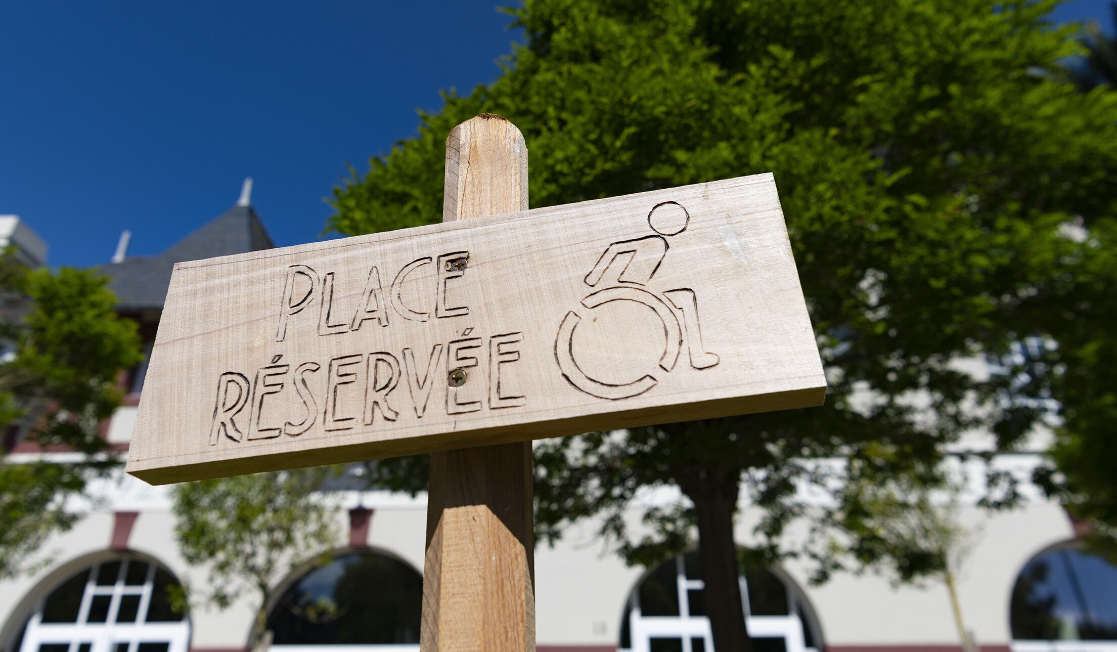 A wooden sign with "PLACE RÉSERVÉE" and a wheelchair symbol, indicating a reserved parking spot.