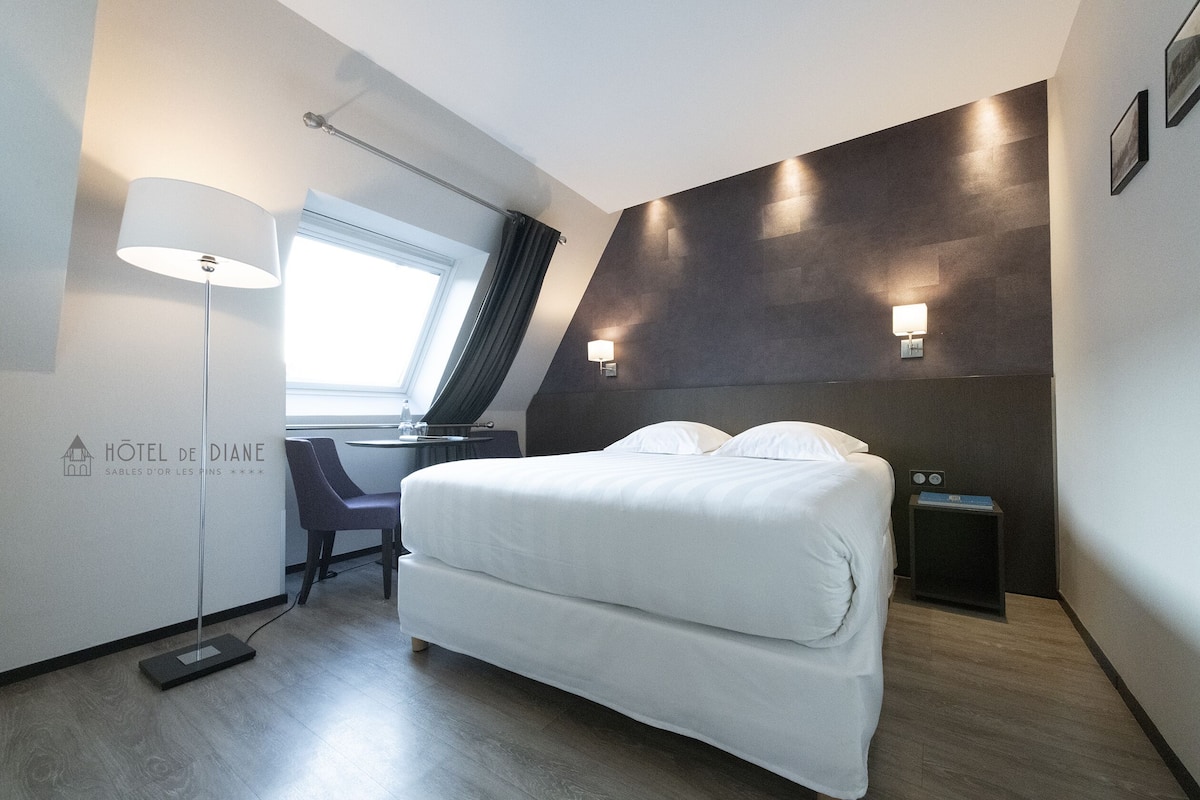 Una habitación de hotel con cama, escritorio, silla, lámpara y mesita de noche.