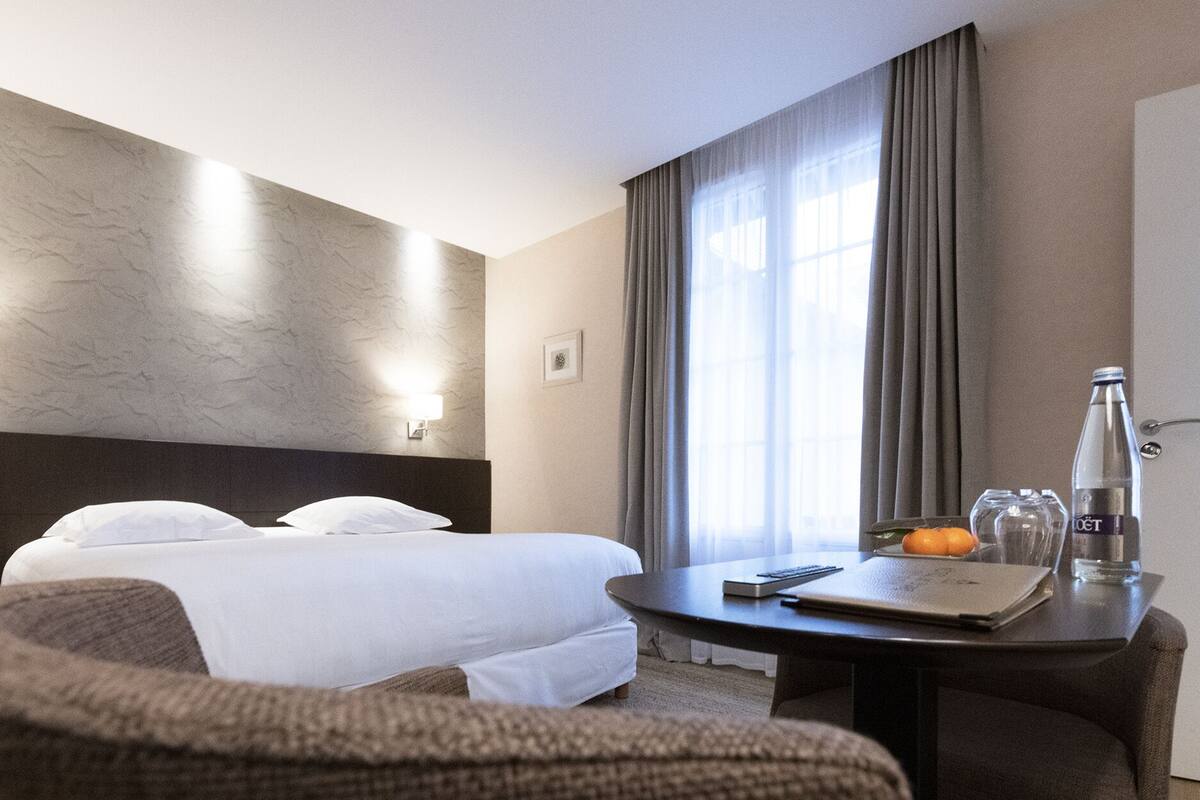 Habitación de hotel con dos camas, un escritorio con una computadora portátil, una botella de agua y un frutero.