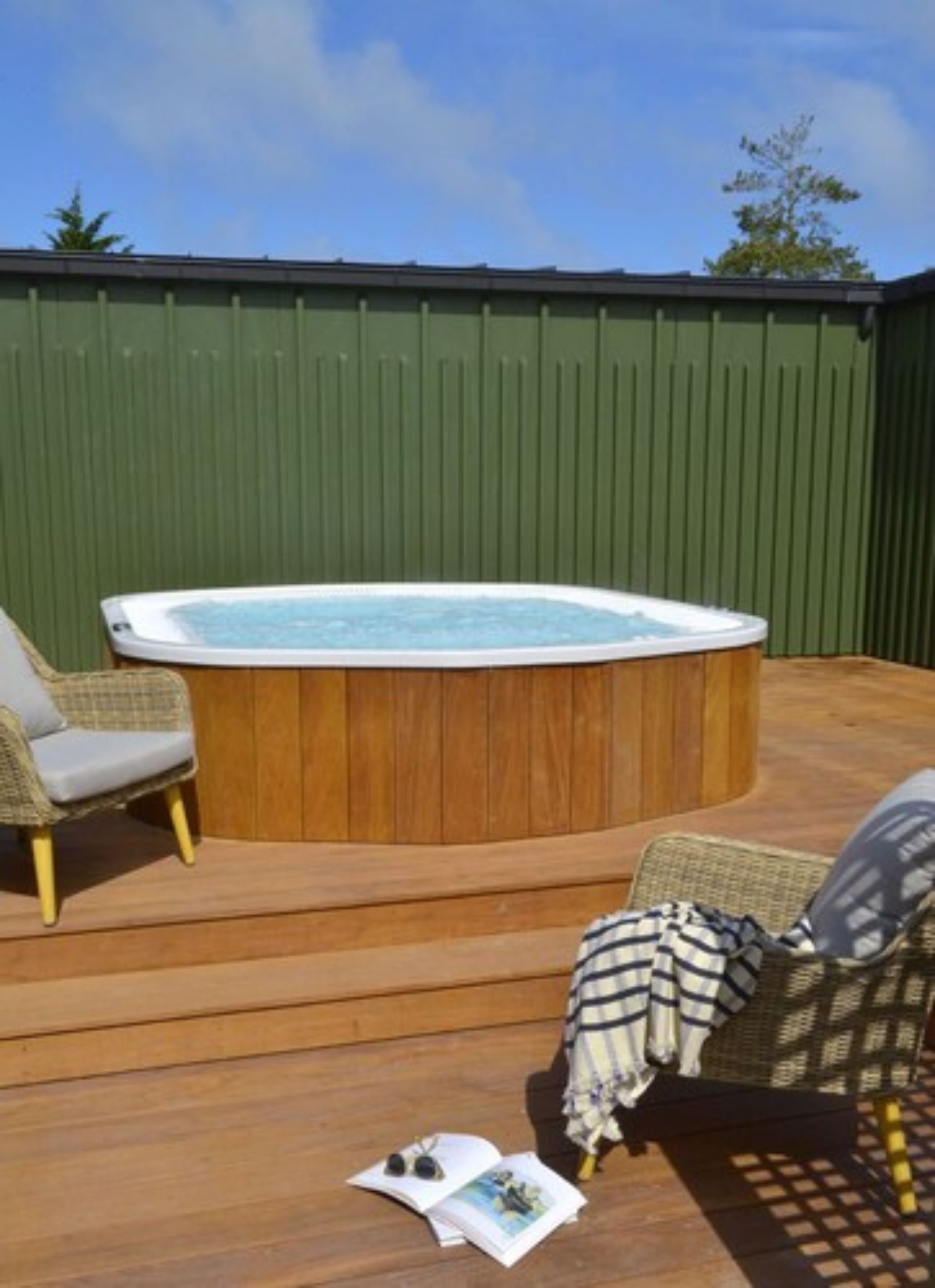A hot tub on a wooden deck with wicker chairs.