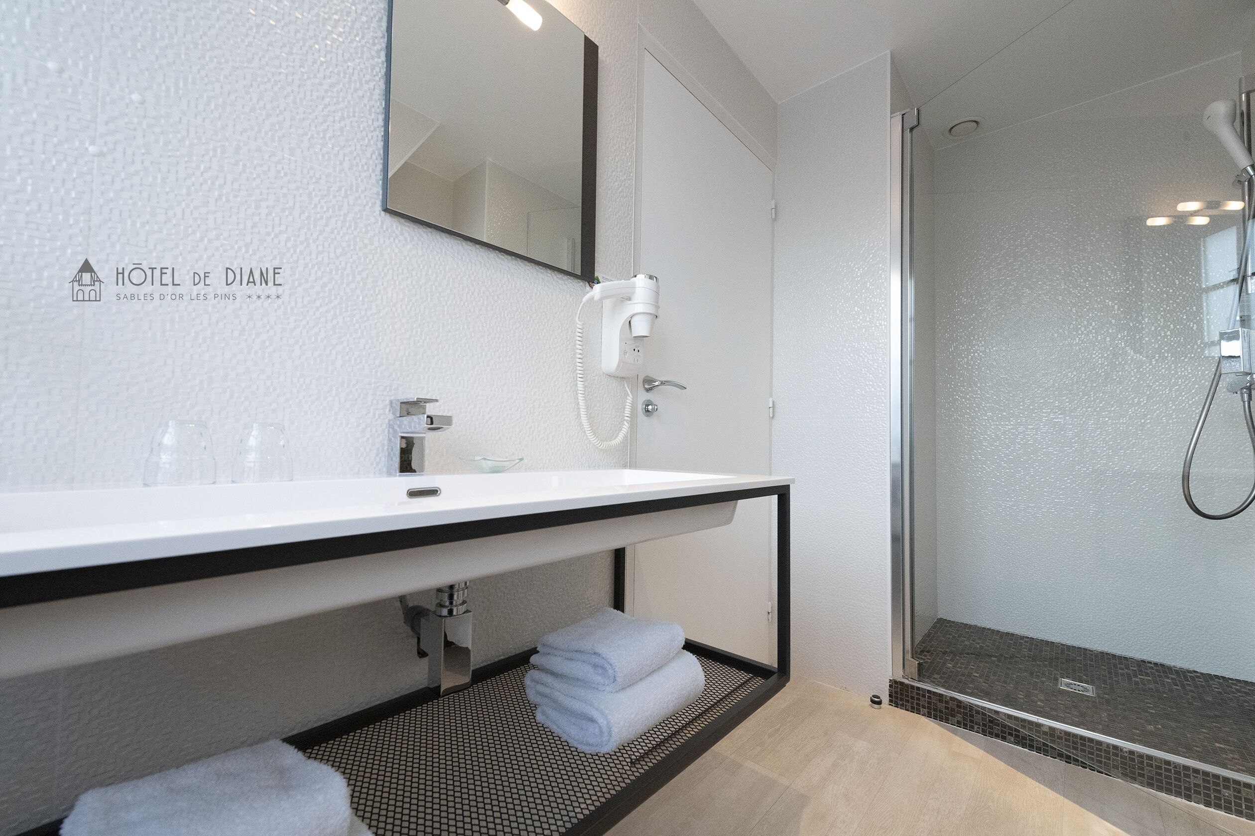A modern bathroom with a white sink, a hairdryer, and a glass shower enclosure.