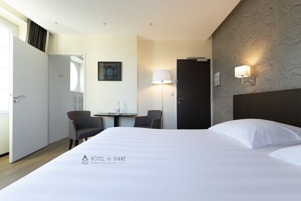 Una habitación de hotel con una cama, dos sillas, una mesita, una lámpara y una puerta.