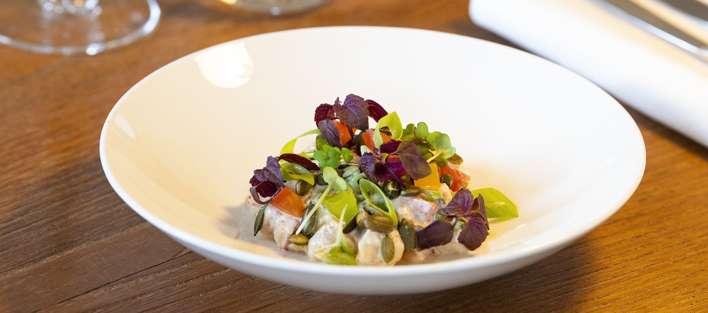 A white bowl of salad on a wooden table.