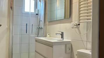 Um banheiro moderno com chuveiro em box de vidro, pia branca com espelho acima e vaso sanitário com dispensador de papel toalha.