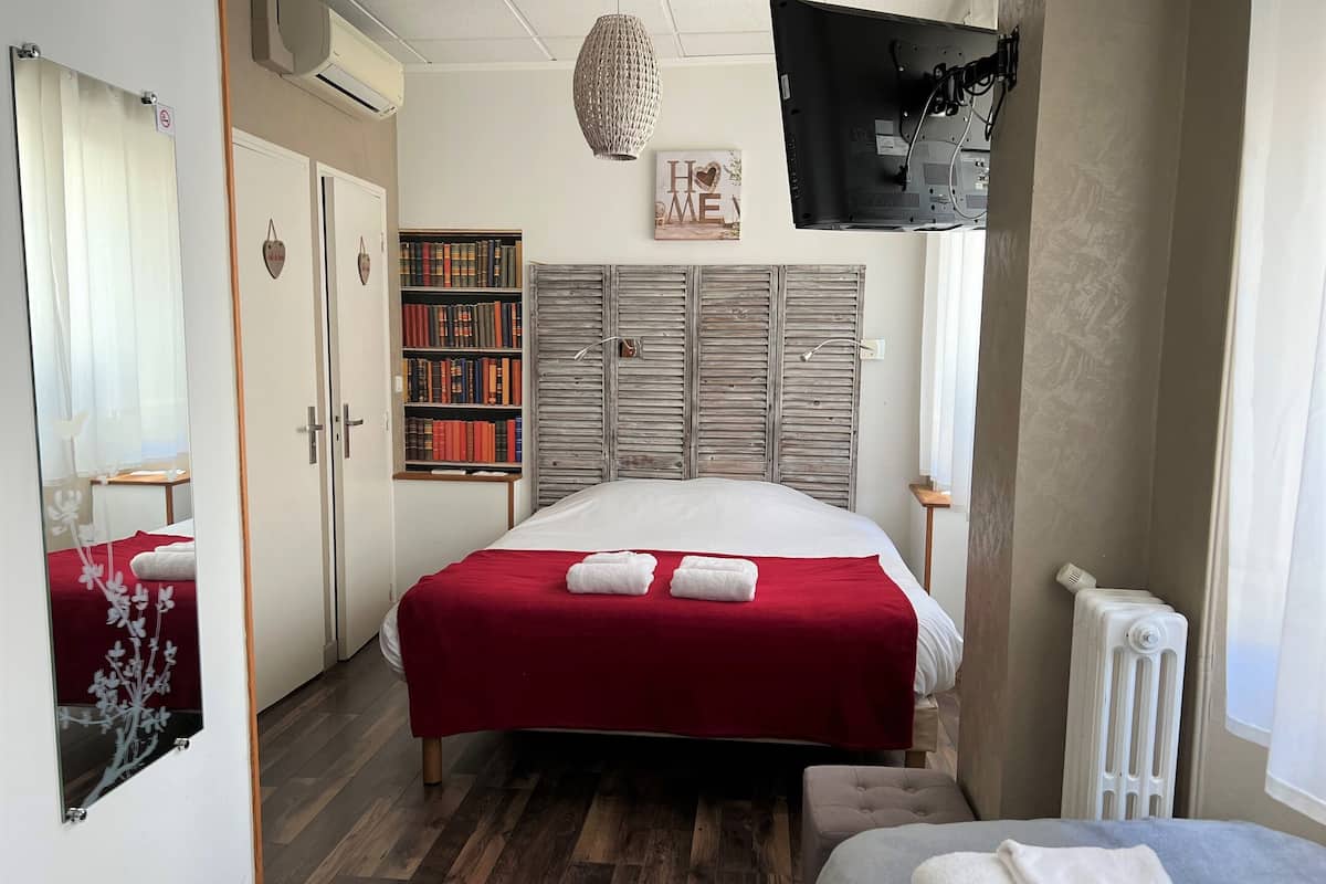 A hotel room with a bed, a bookshelf, a wardrobe, and a TV mounted on the wall.