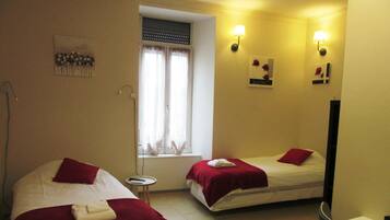 Habitación de hotel con dos camas, cada una con una colcha roja, una mesita redonda con un control remoto y una ventana con cortinas.