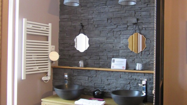 A bathroom with a stone wall, two black sinks, a wooden vanity, and pendant lights.