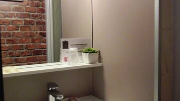 A bathroom with a white sink, a mirror, a small potted plant, and a coffee maker on the countertop.