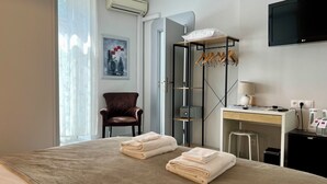 A hotel room with a bed, a chair, a desk with a lamp, a TV, and a wardrobe.
