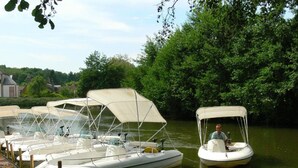 Une rangée de petits bateaux est amarrée à un quai, avec une rivière paisible et une végétation luxuriante en arrière-plan.