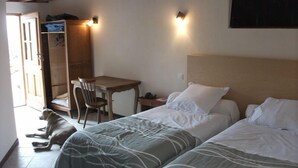 Une chambre avec deux lits, un bureau, une chaise et un chien.