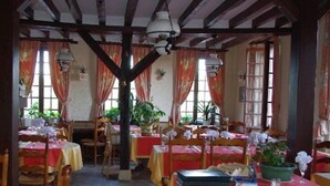 Un espace repas agrémenté de poutres en bois, de tables recouvertes de nappes rouges et de plantes en pot.
