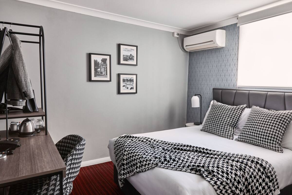 Une chambre d’hôtel équipée d’un lit, d’un bureau, d’une chaise, d’un porte-manteau et de tableaux accrochés au mur.