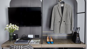 Una habitación moderna con una televisión de pantalla plana, un escritorio con un jarrón de flores, una revista, un par de zapatos y un abrigo colgado en un perchero.
