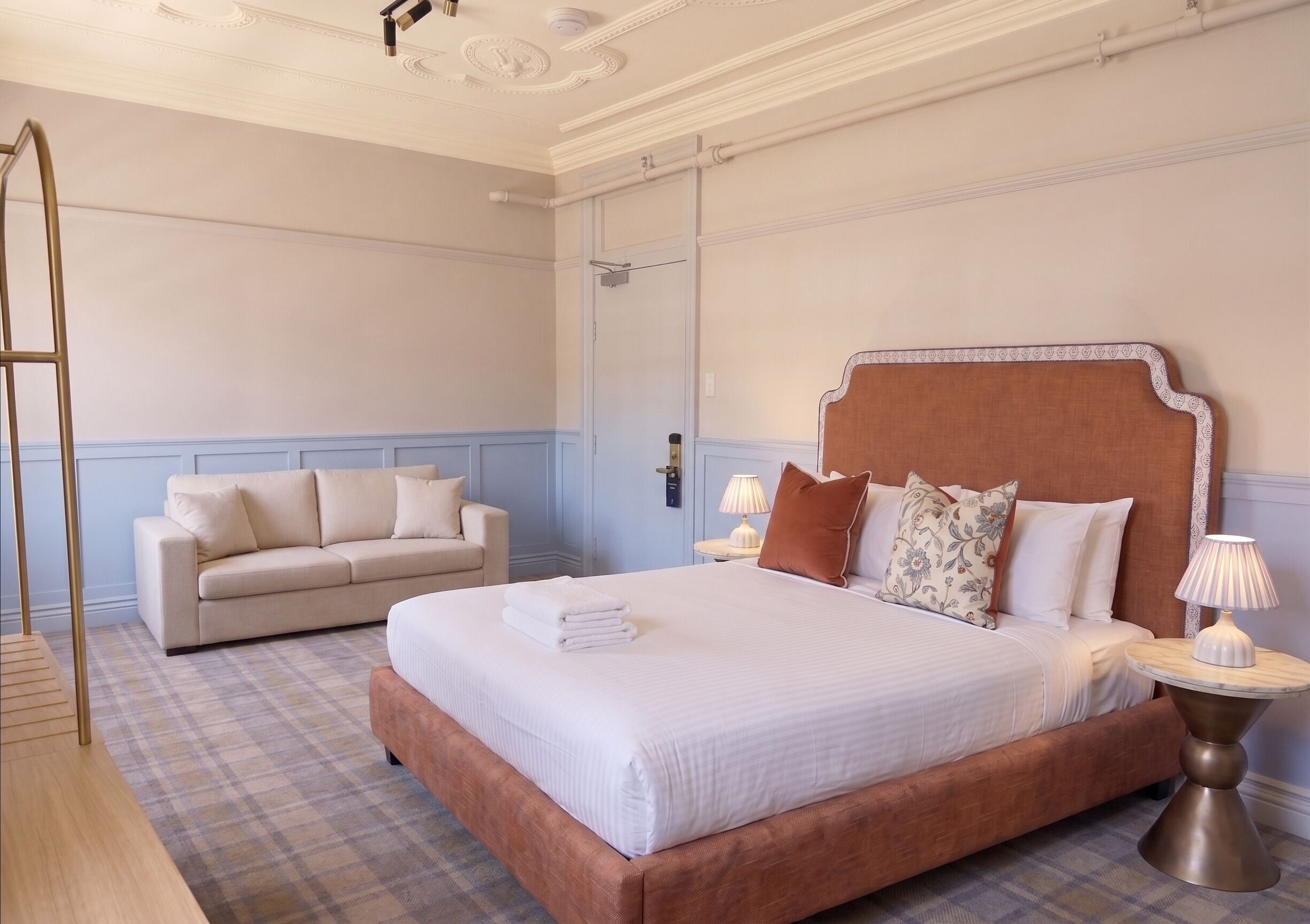Habitación de hotel con una cama grande, un sofá, dos mesitas de noche con lámparas y un espejo en la pared.