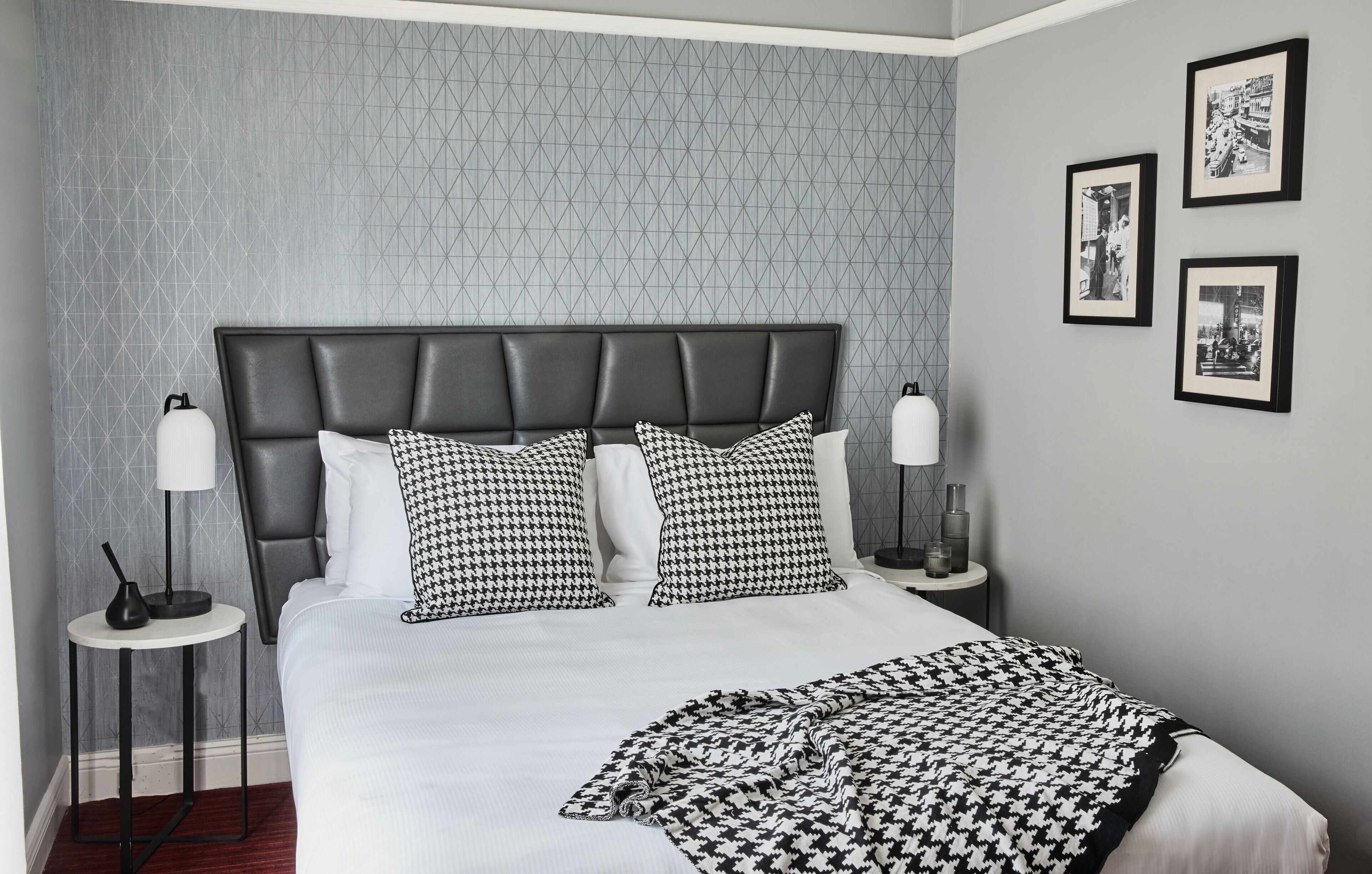 A neatly made bed with a black and white patterned headboard, two bedside tables with lamps, and three framed pictures on the wall.