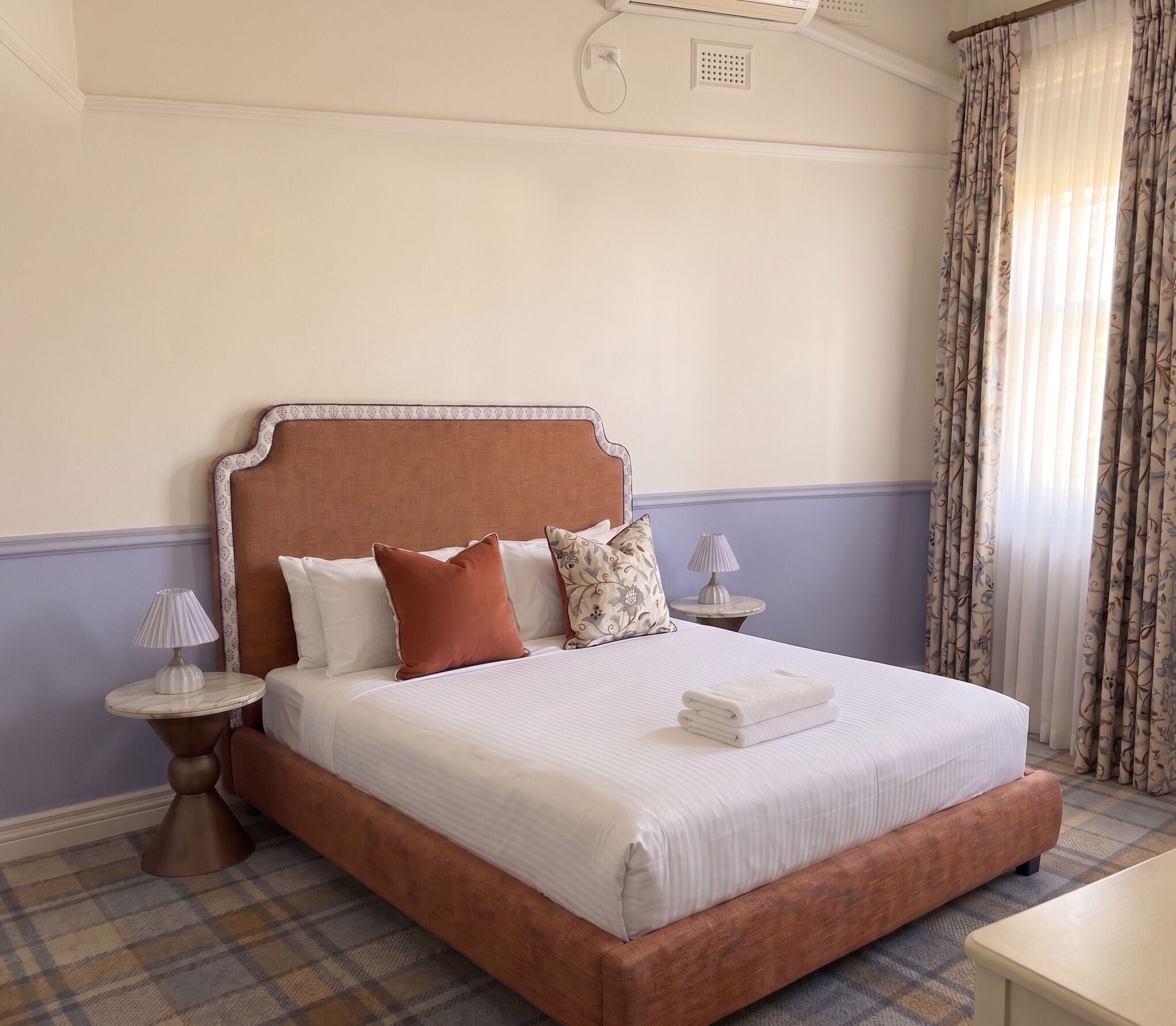 A neatly made bed with a headboard, a bedside lamp, and a folded towel on the bed.