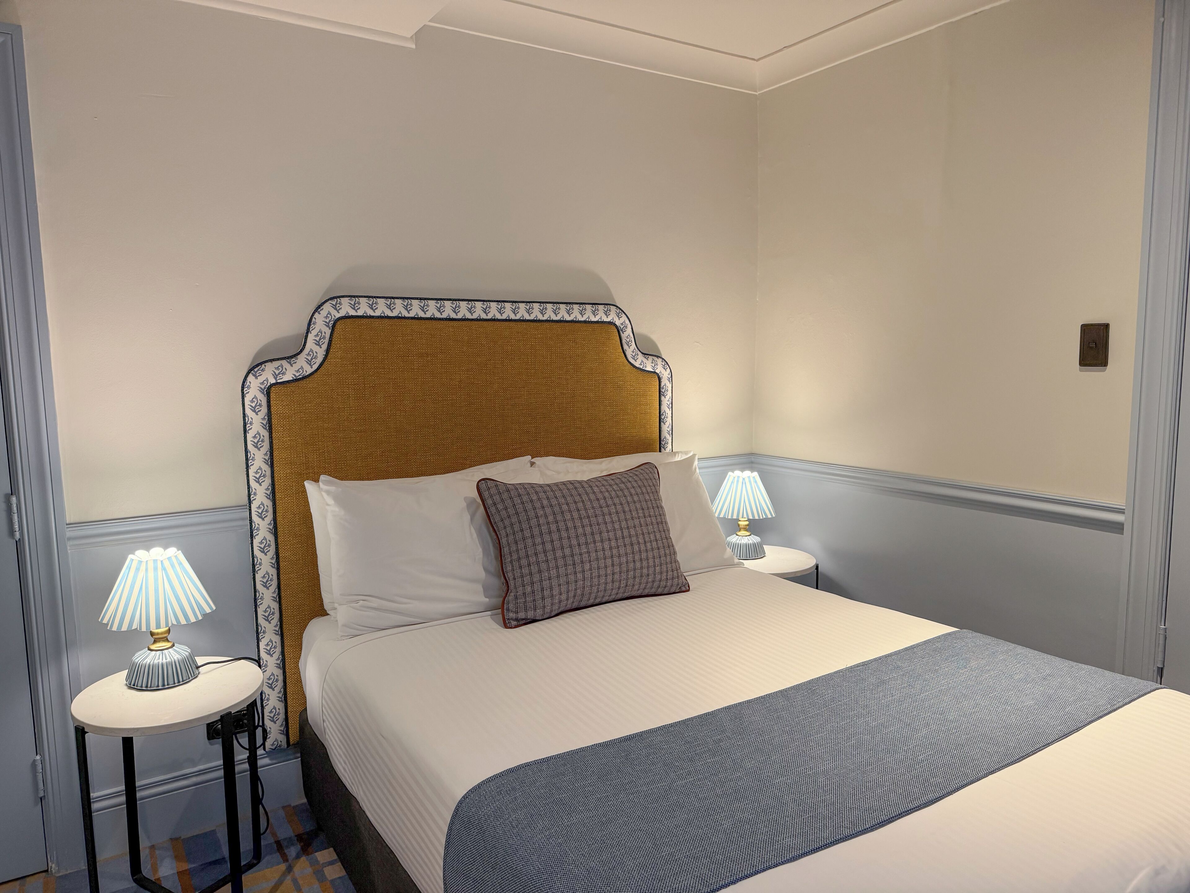A neatly made bed with a headboard, two bedside tables with lamps, and a patterned rug on the floor.