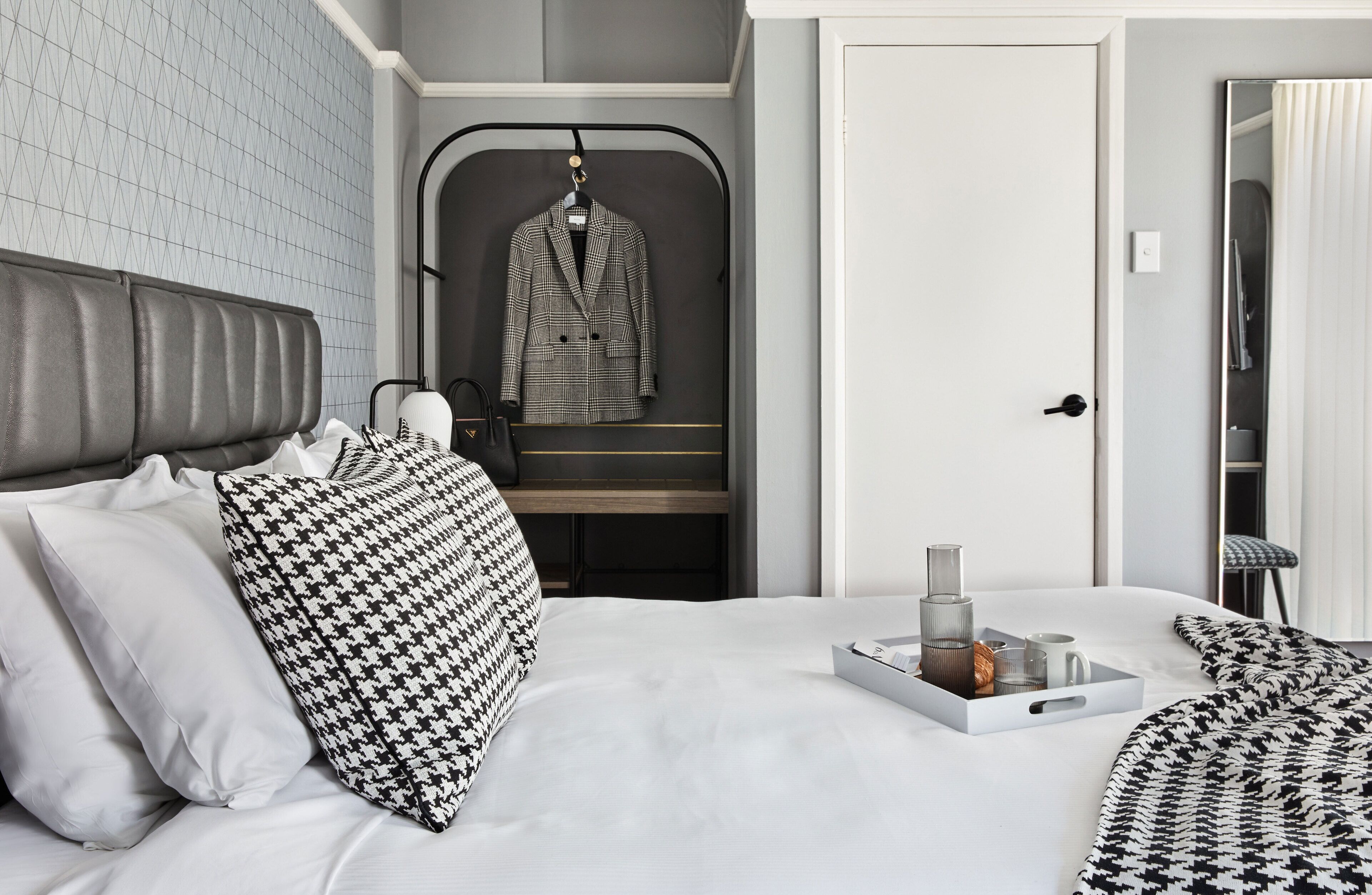 A hotel room with a bed, a hanging coat rack, a tray with toiletries, and a mirror.