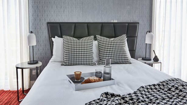 Una cama bien hecha con una bandeja de alimentos para el desayuno, incluyendo un croissant, un vaso de agua y una taza de café.