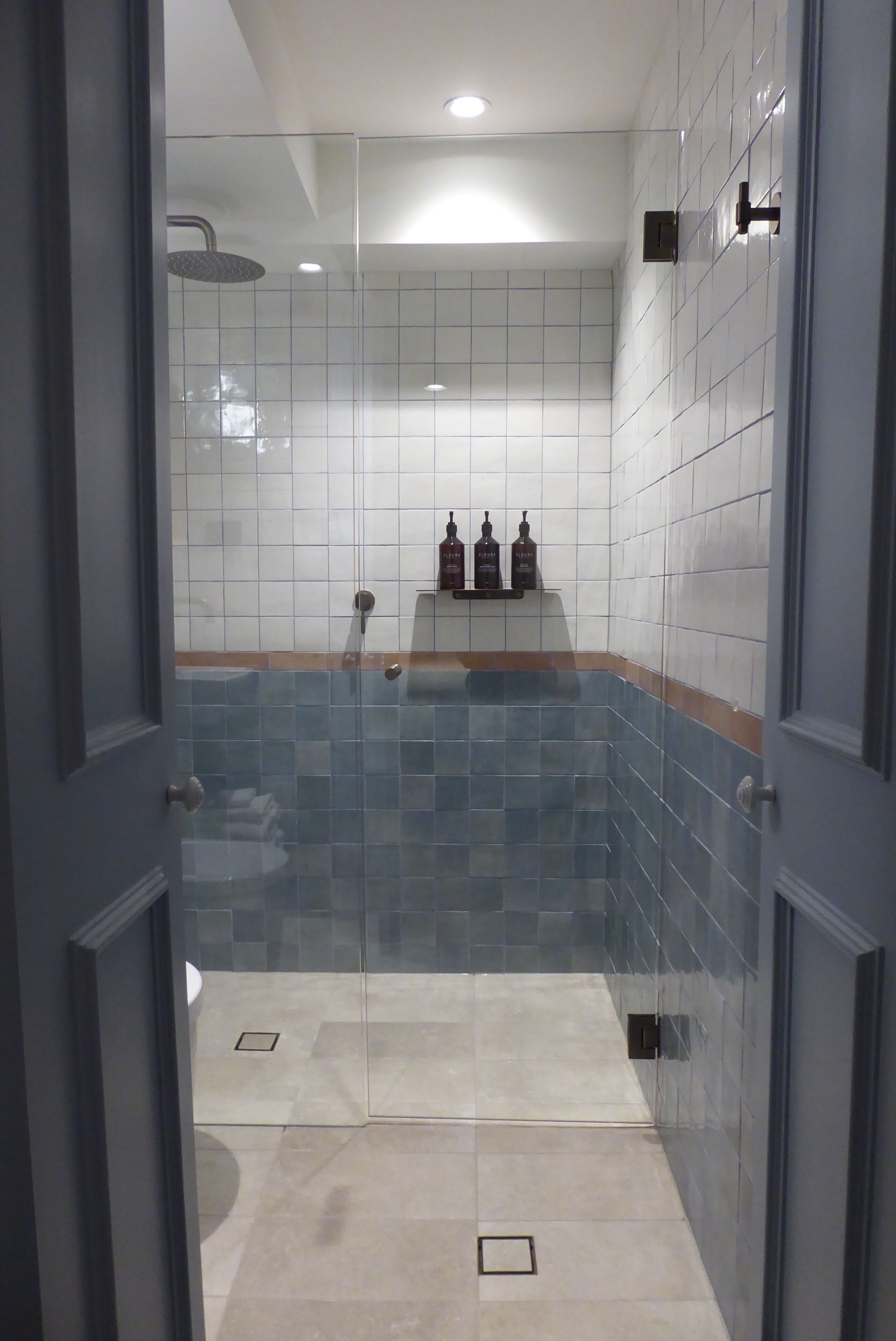 A bathroom with a glass shower enclosure, tiled walls, and a shelf with toiletries.