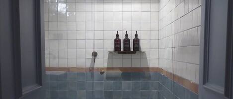 A bathroom with a glass shower enclosure, tiled walls, and a shelf with toiletries.