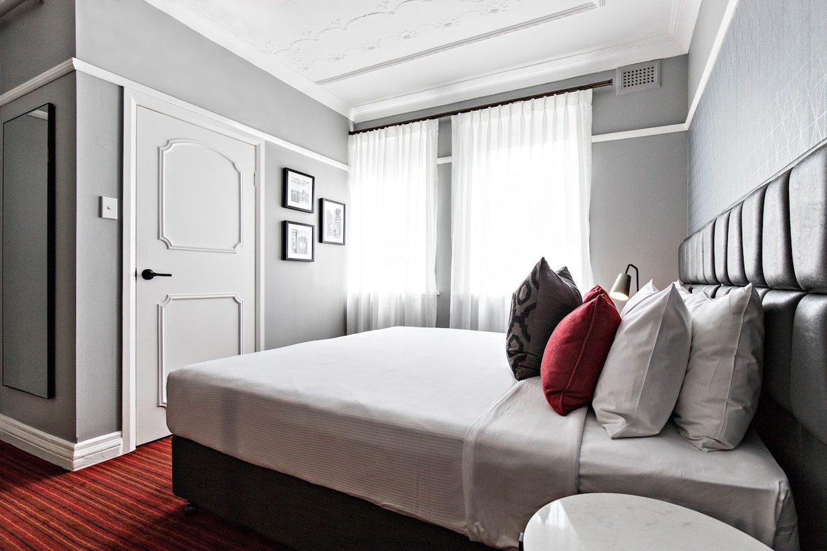 Habitación de hotel con una cama grande, un armario y una ventana con cortinas.