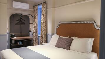 Una camera d'albergo con un letto, una scrivania con una sedia, un appendiabiti e una finestra con tende.