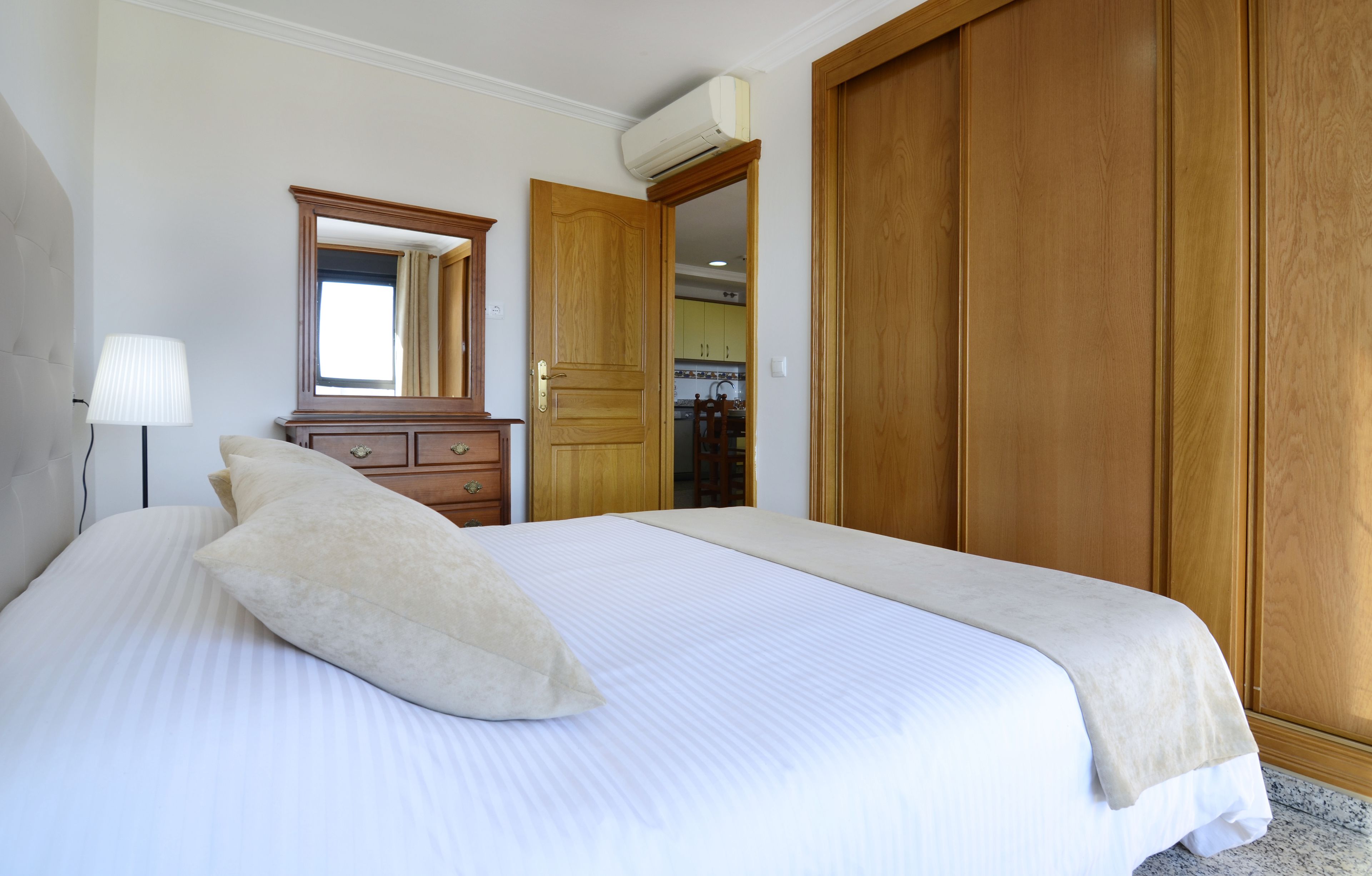 A bedroom with a large bed, a dresser, a mirror, and a wardrobe.